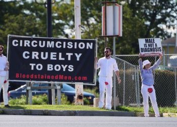 Standing outside Centura Health Primary Care in Thornton, Colorado, on April 6, two men dressed in all-white garb — except for a significant, blood-red mark on the crotch of their pants — faced traffic and held a large sign saying, "CIRCUMCISION PENIS MUTILATION."
